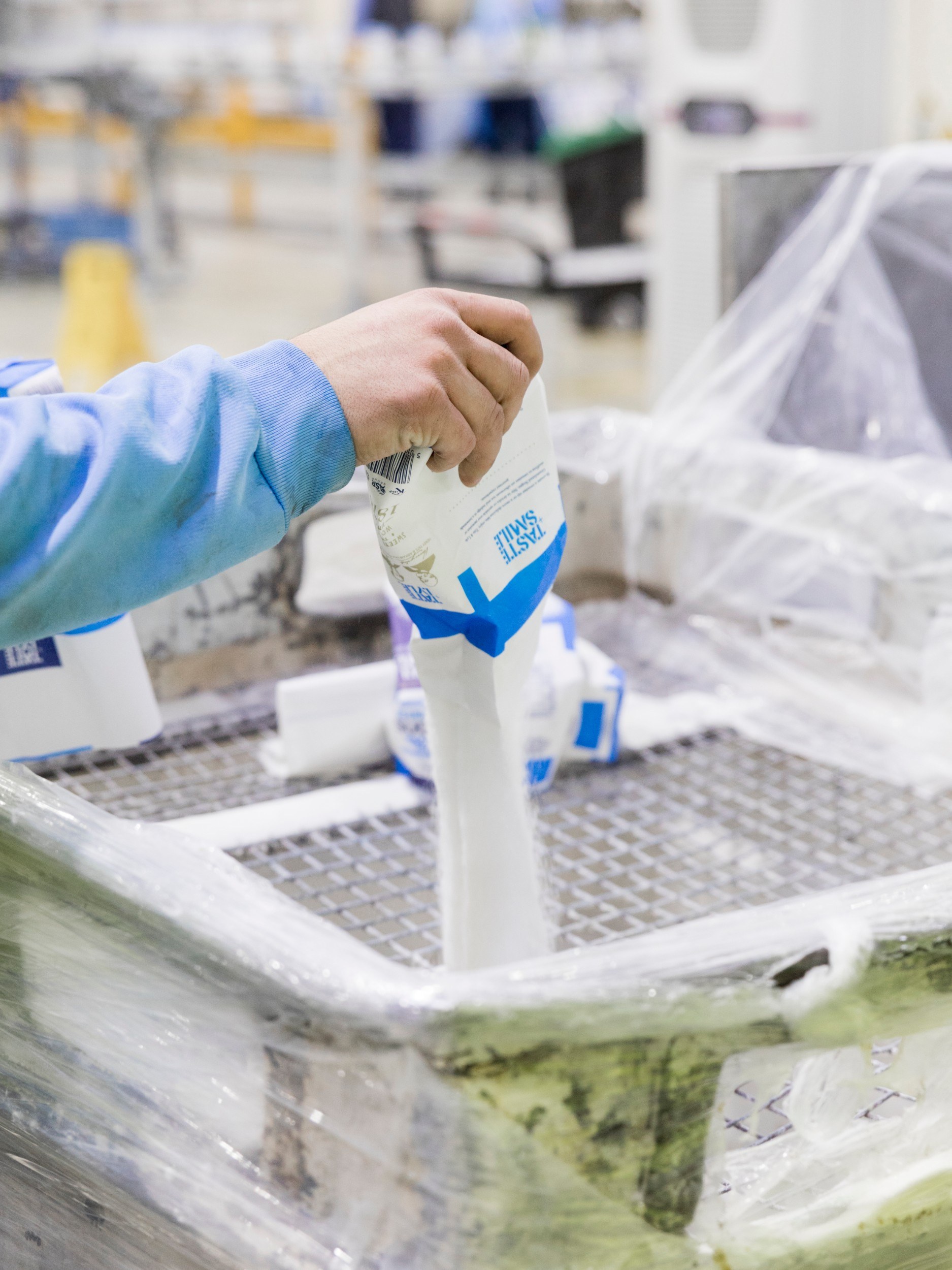 Bag of sugar being poured into a mesh. The worker's hand is visible.