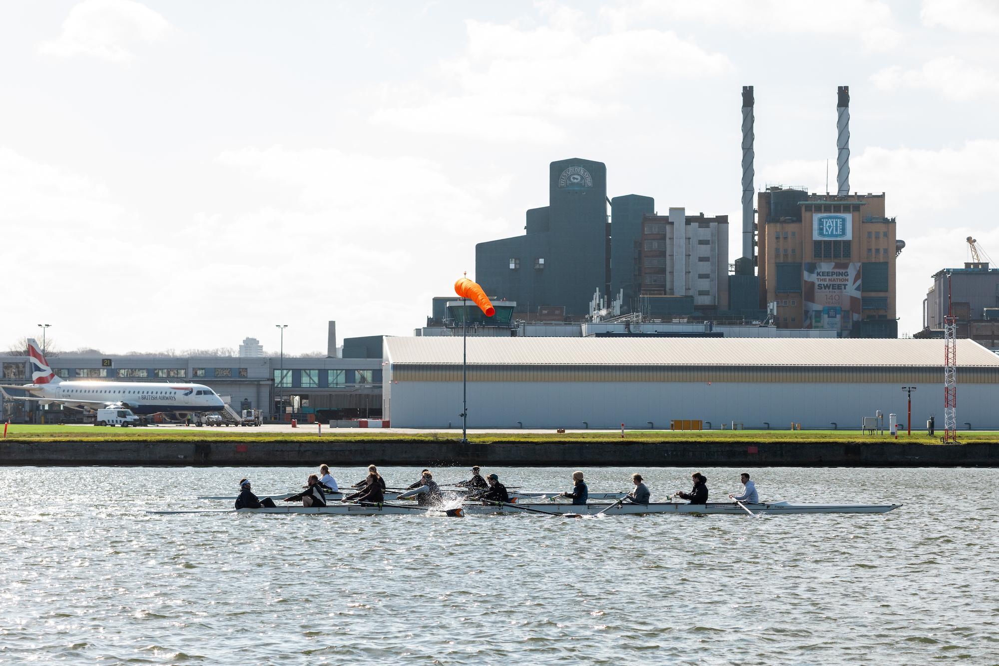 rowers on the water with city airport and tate and lyle factory in the background