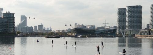 Seven people in wetsuits paddleboarding on the water at the Royal Docks