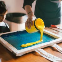A yellow pot of paint being poured on a board