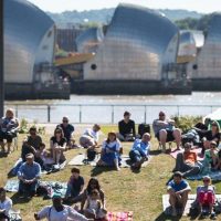 Image shows people sitting on the grass at Thames Barrier Park, enjoying an event.