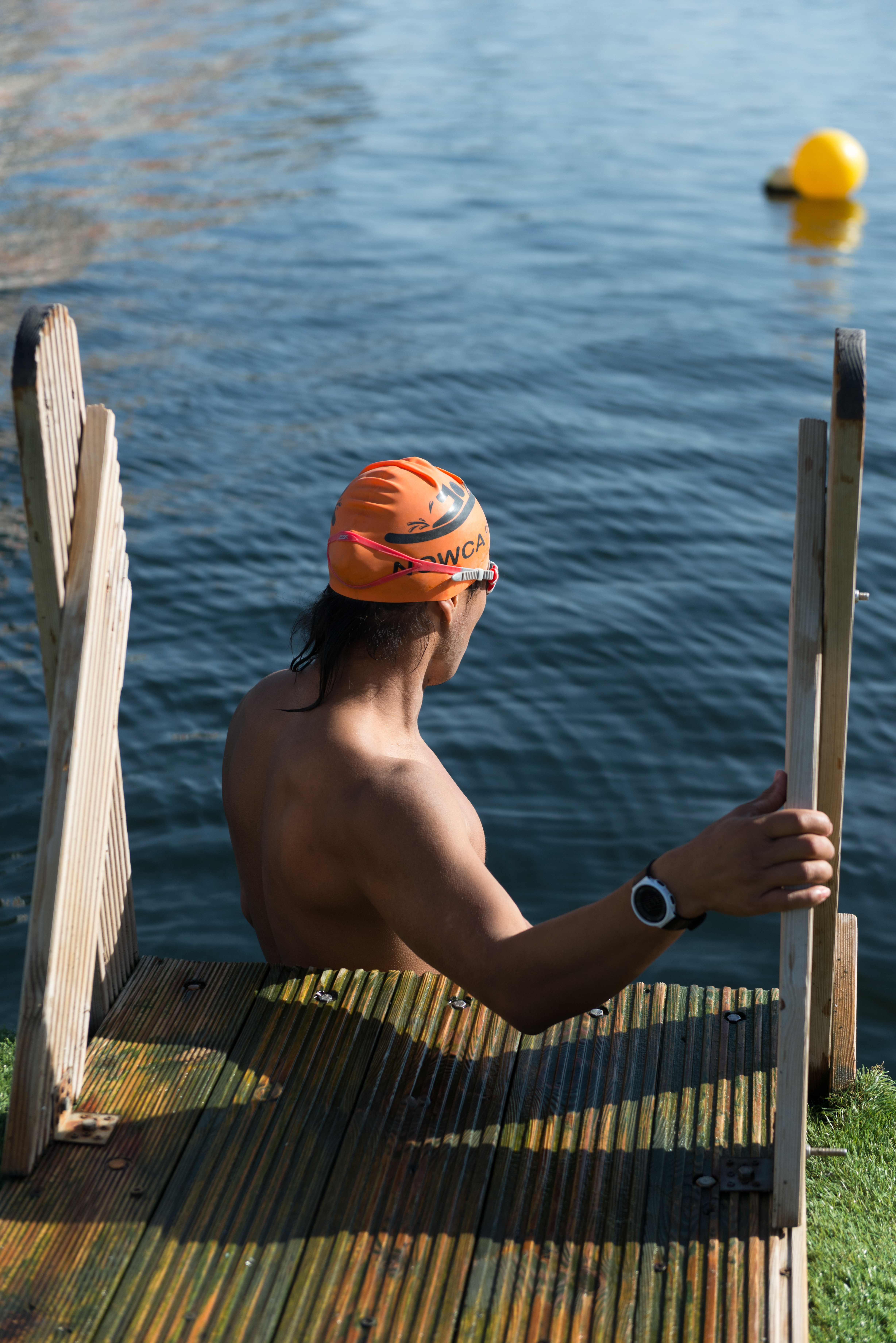 A swimmer in an orange cap about to set out from the dock edge