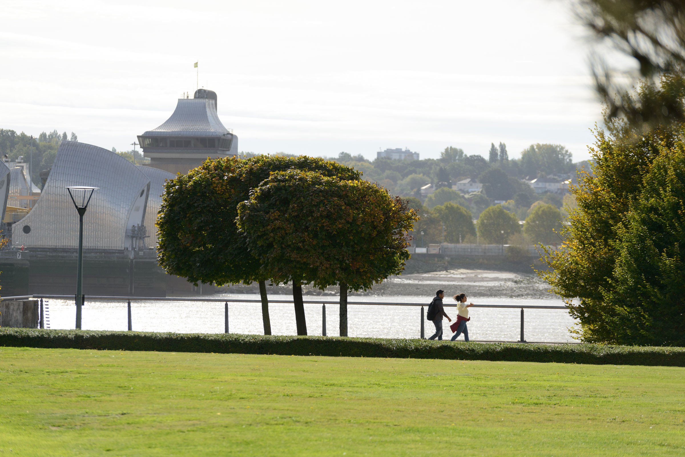 People walking in Thames Barrier Park with the river as backdrop