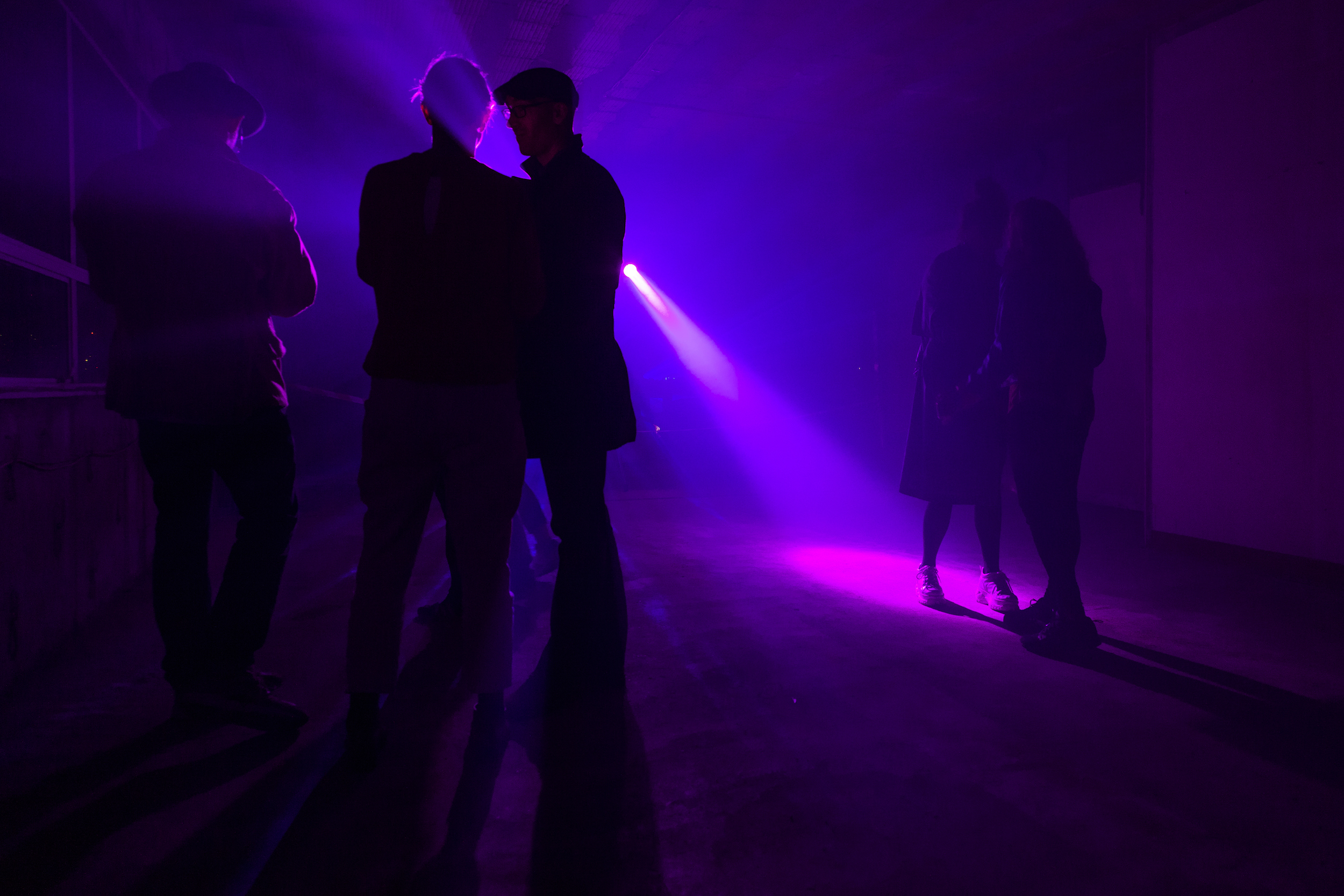 Dark room with purple lighting and silhouettes of a few people in the foreground