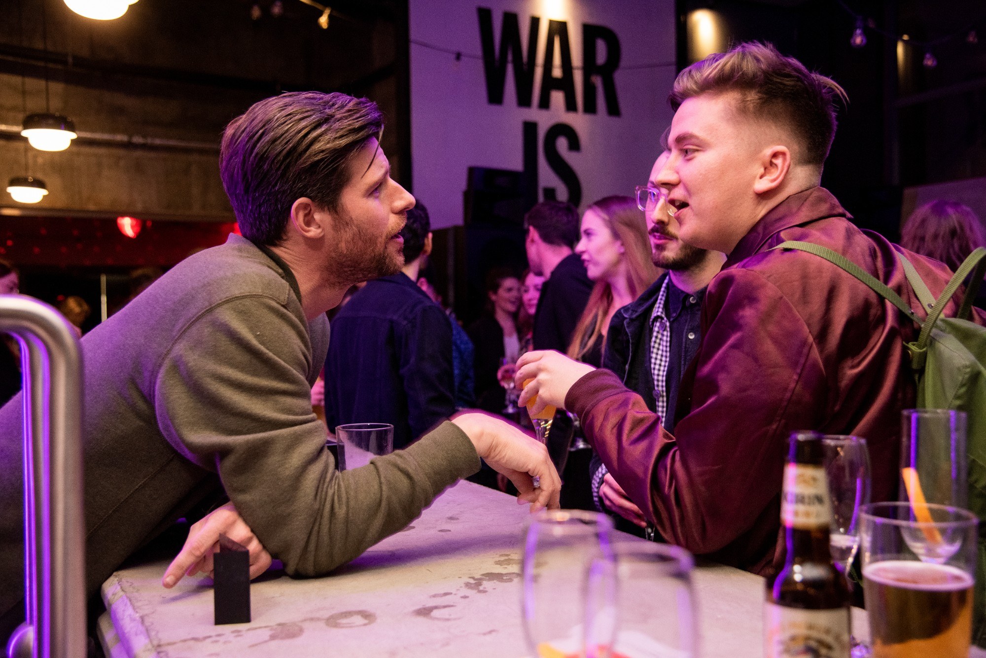 Two men leaning over a bar, in animated discussion. Drinks in foreground