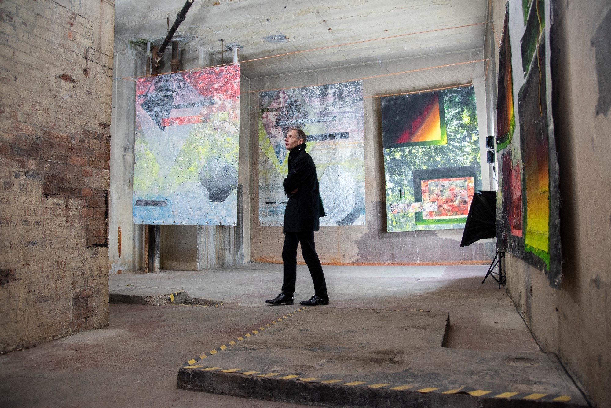 Man looking at large abstract paintings in room with concrete walls