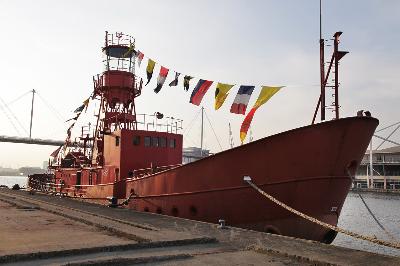 Red boat with lighthouse tower and flags moored on the edge of the dock