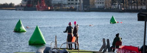 Two swimmers in wetsuits ready to dive into the dock water