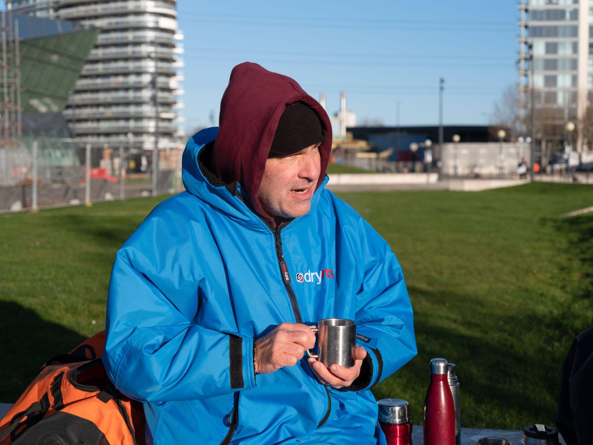 A swimmer in a robe drinking tea post swim