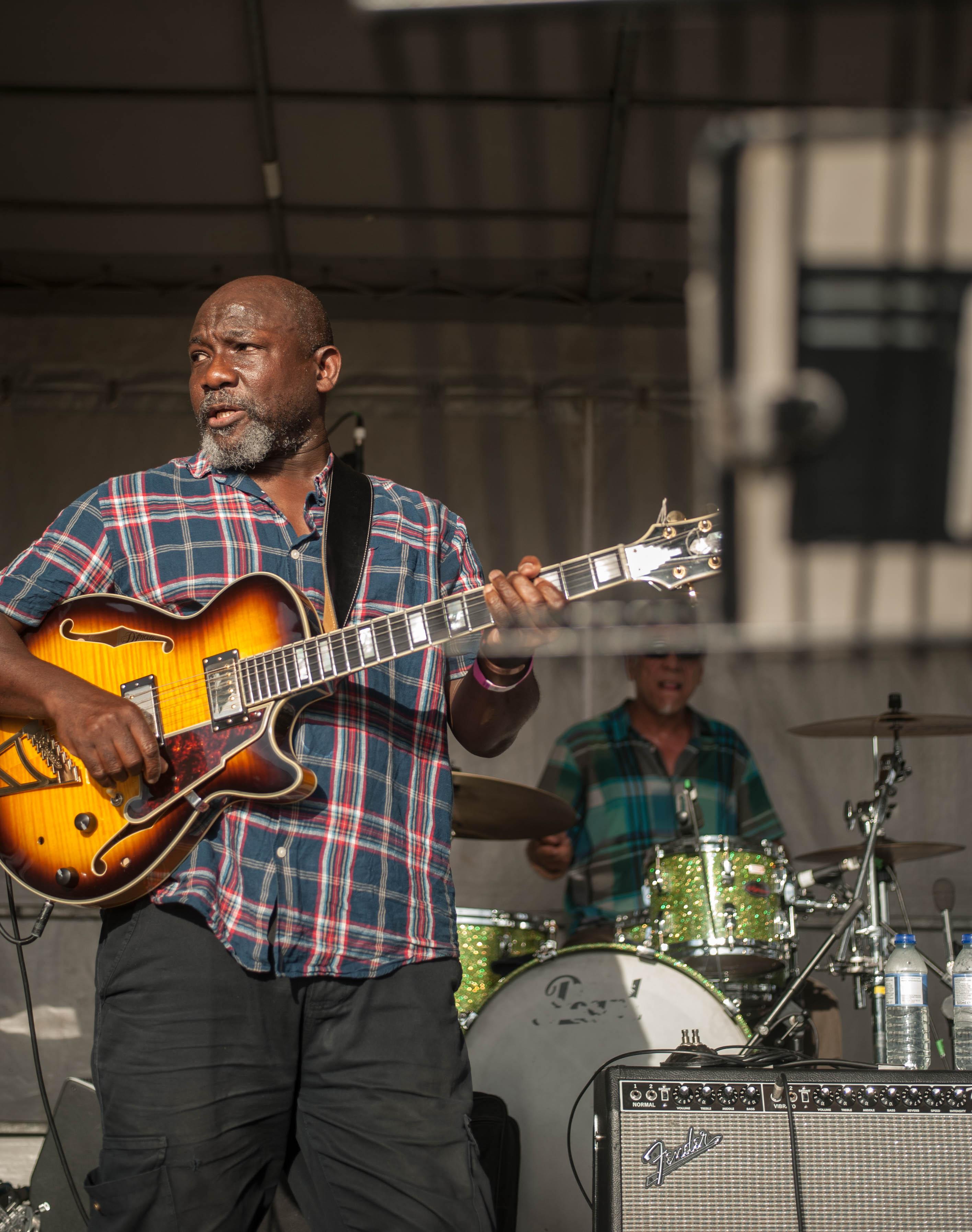 A man playing guitar on stage with a drummer in the background