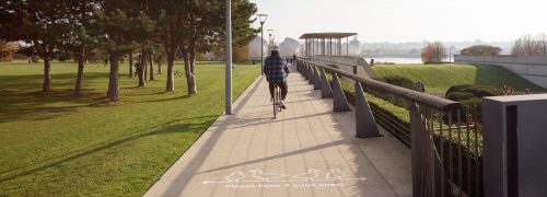 Cyclist in Thames Barrier park with text on ground reading 'please keep four gulls apart'