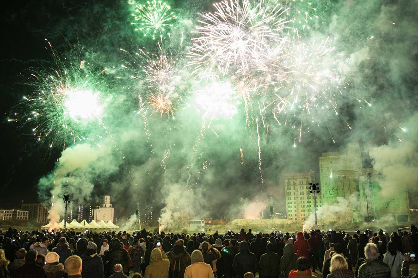 Bright green and white fireworks exploding over a large onlooking crowd