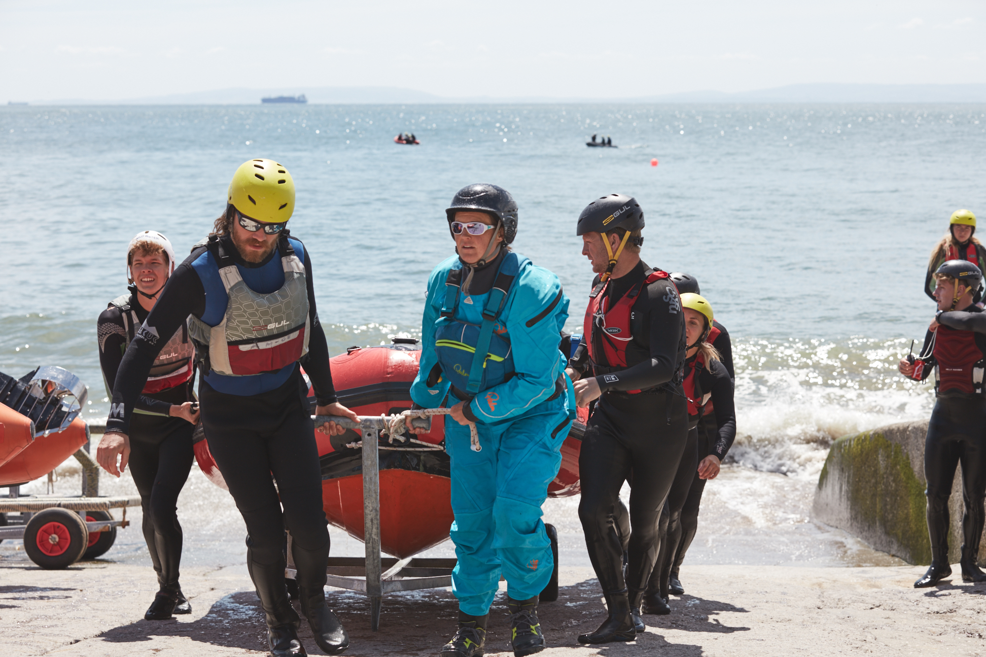 A group of people in wetsuits and lifejackets bringing a lifeboat out of the water