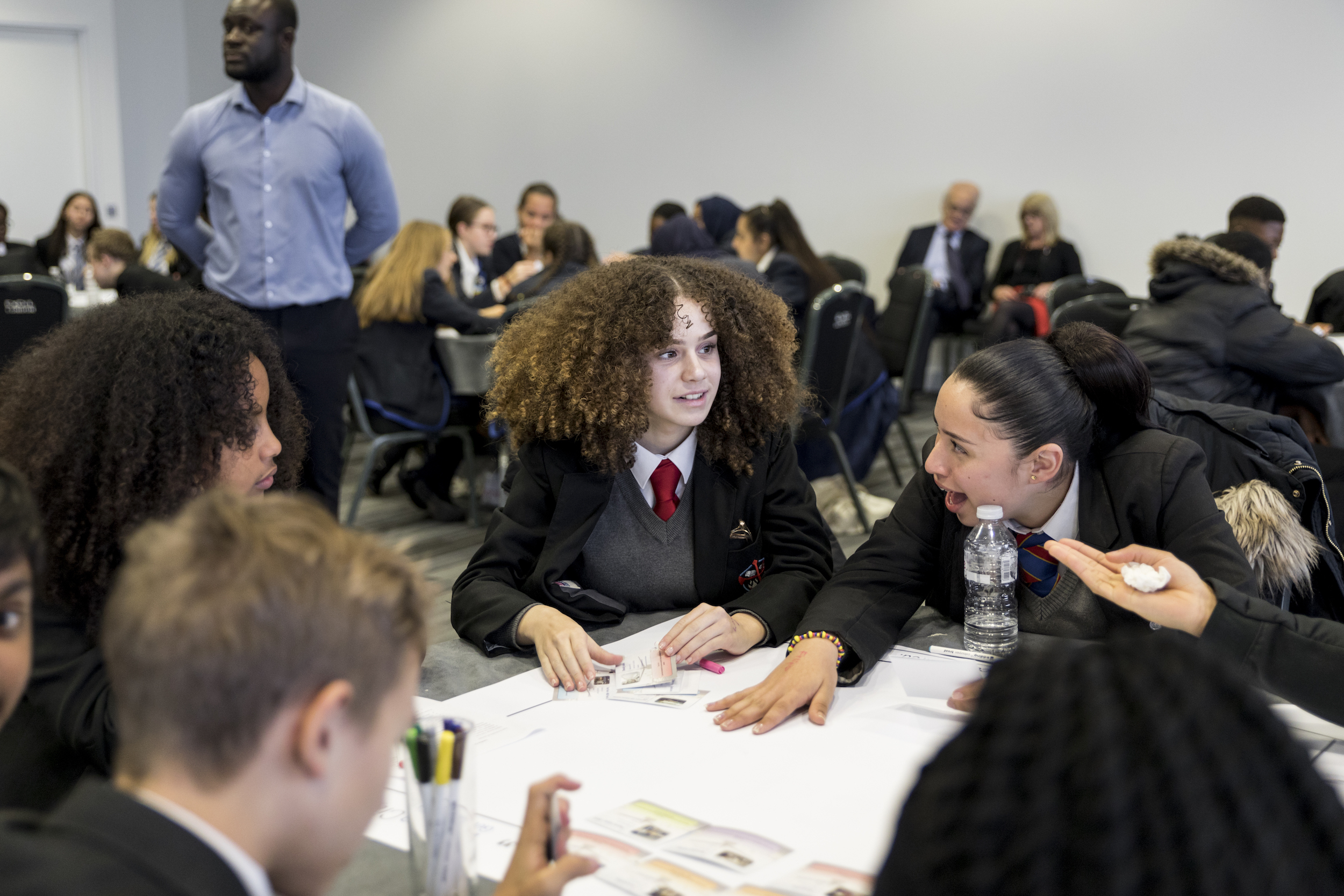 Children sitting around a table with a large airport diagram in front of them; one girl is exclaiming in surprise