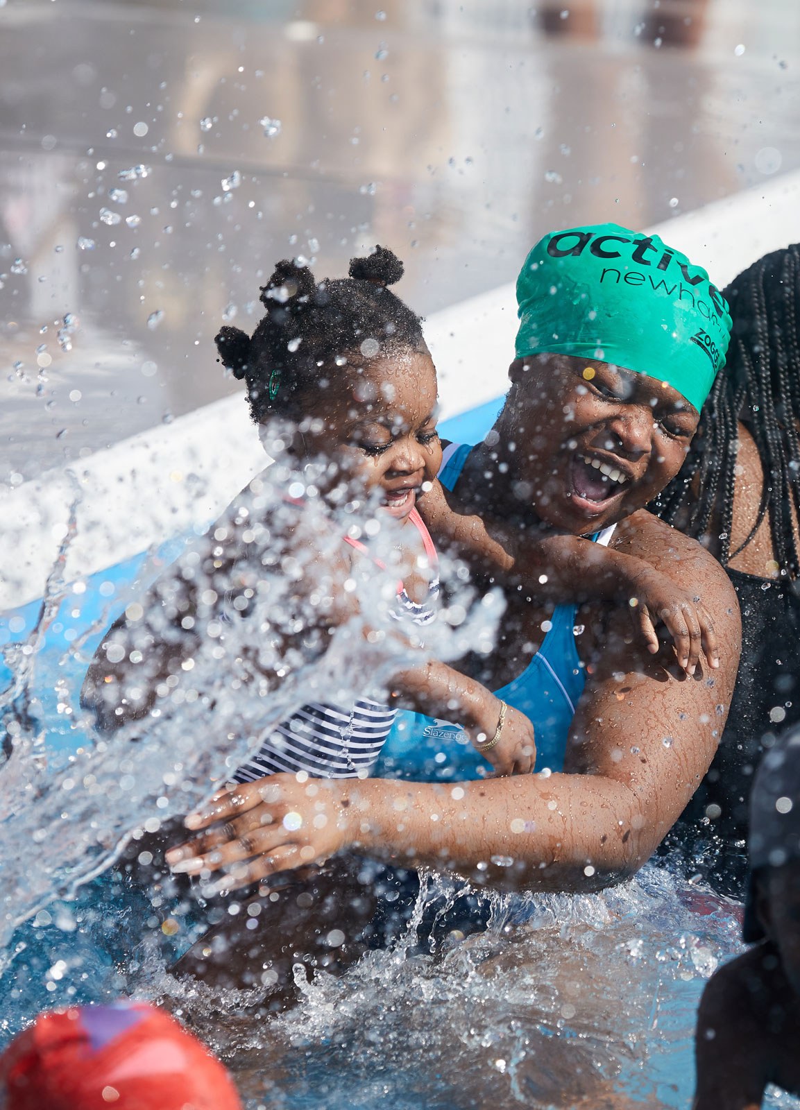 A woman with a child in swimwear, laughing while caught in a splash