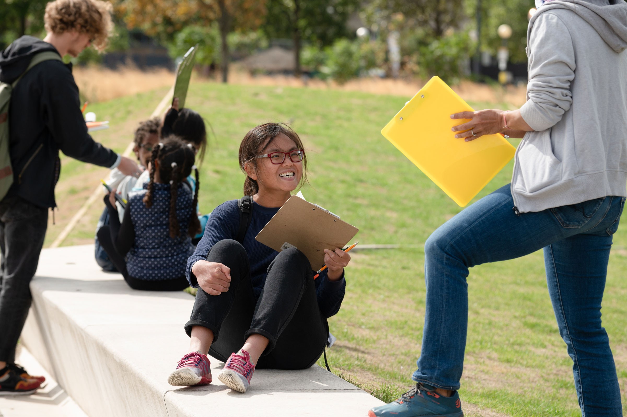 Children sitting on benches, a girl with a notepad smiling