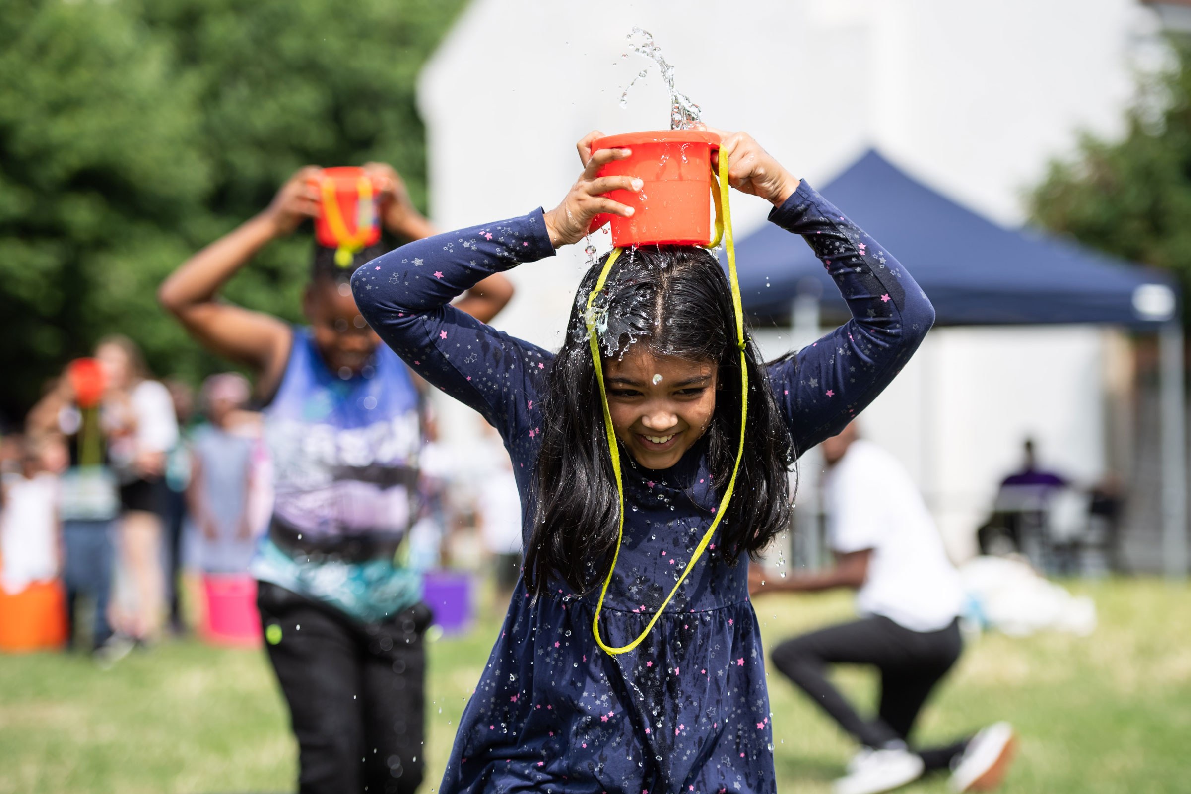 A girl with a bucket of water on her head, laughing
