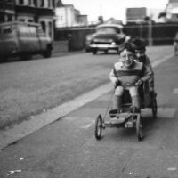 Black and white photo of two young boys go-karting on the street