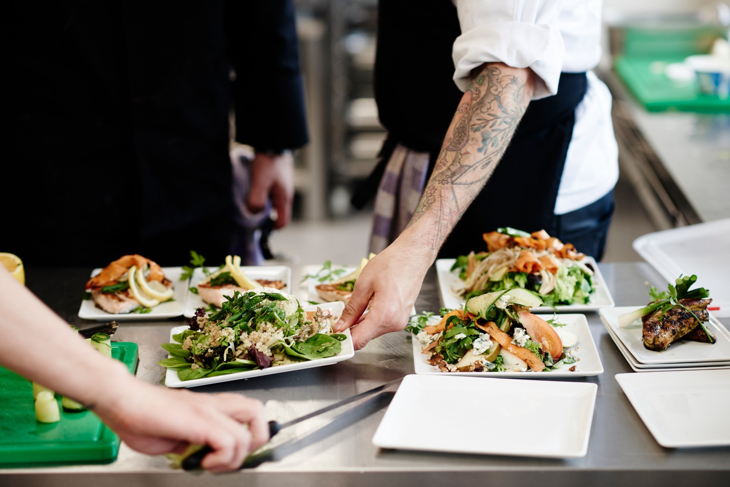 Multiple plates of food. One plate of food is being picked up by a chef.