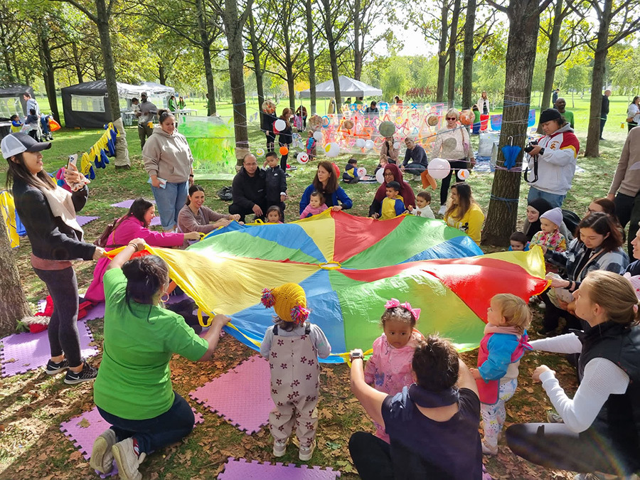 A group of families and children playing with a colourful parachute in a park.