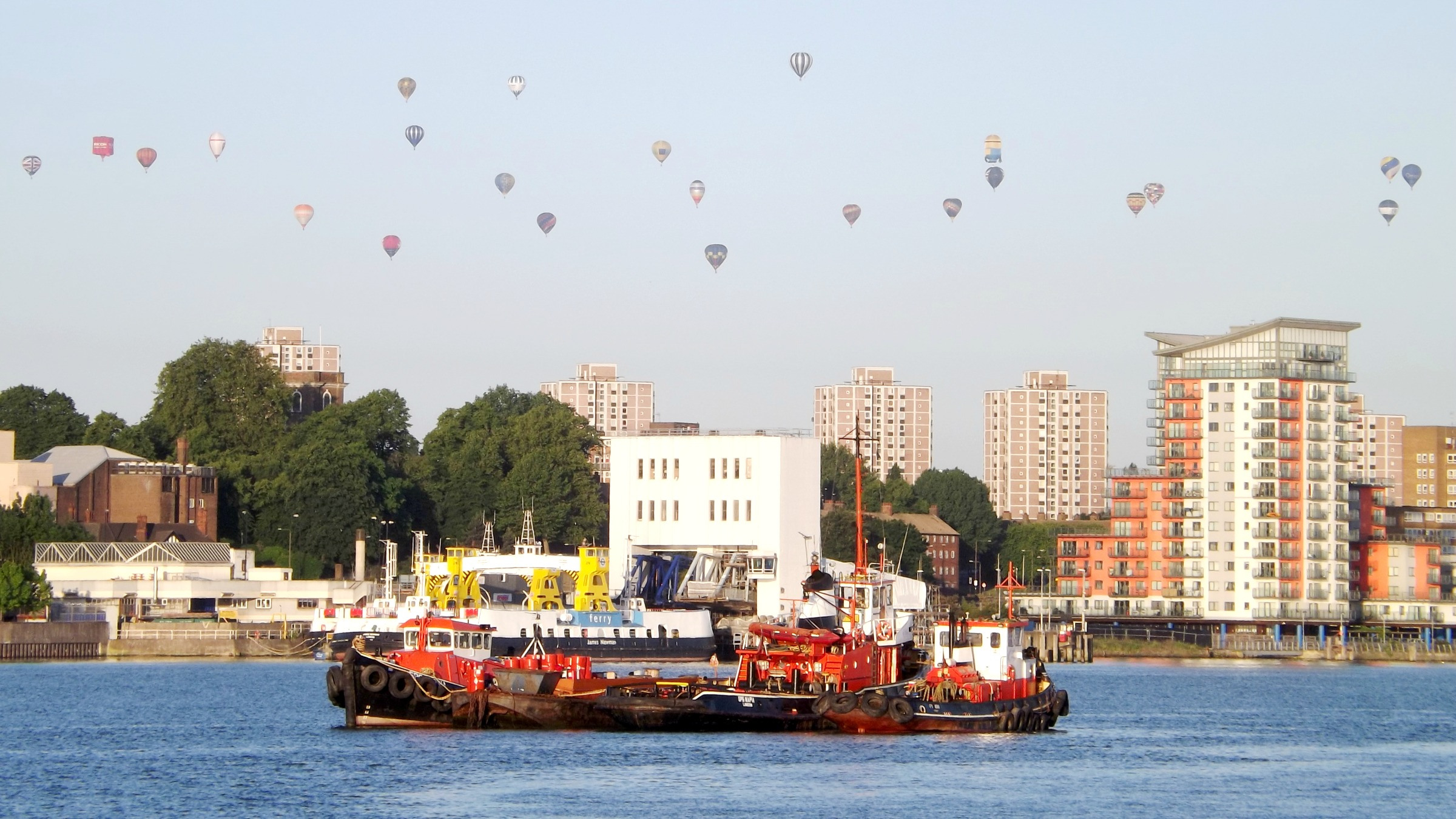 A large group of hot air balloons flying over the Royal Docks