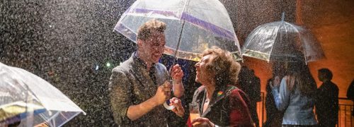 Man and woman under an umbrella in the flavour rainbow, both laughing