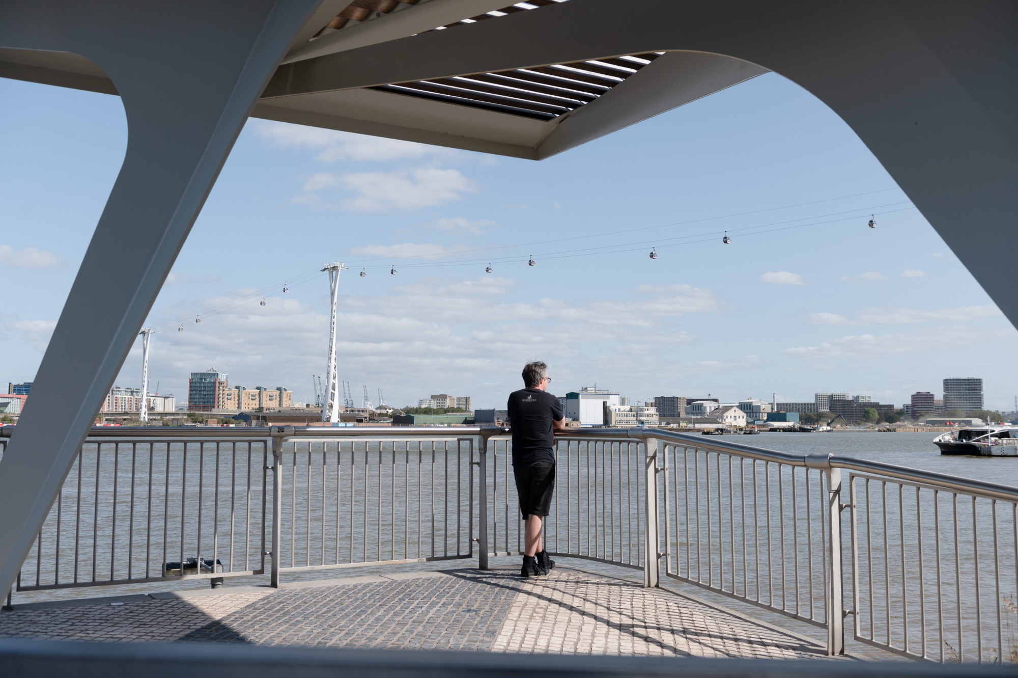 Man looking out at the river from a covered platform, with the cable car in view