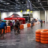 People cycling bikes along an indoor track bordered by tyres